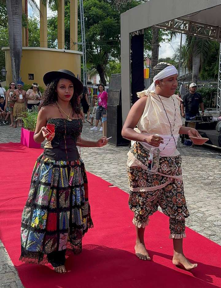 Participantes adultos mostram vestimentas de inspiração afro em desfile cultural da Casa do Axé